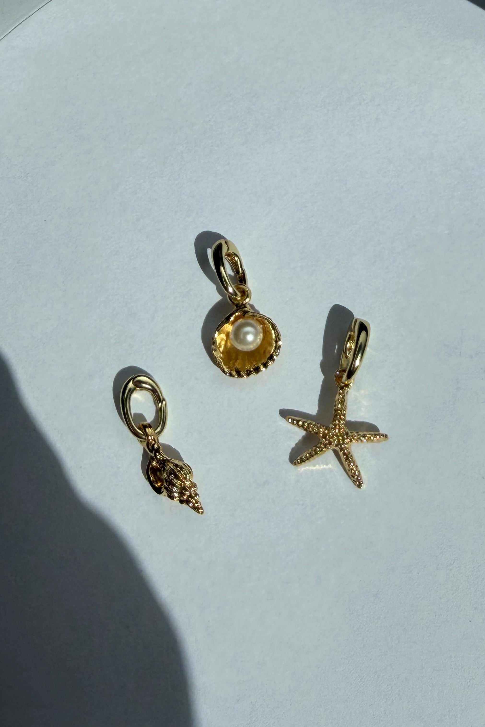 Gold bikini charms including a starfish, clam shell, and conch on a white surface.
