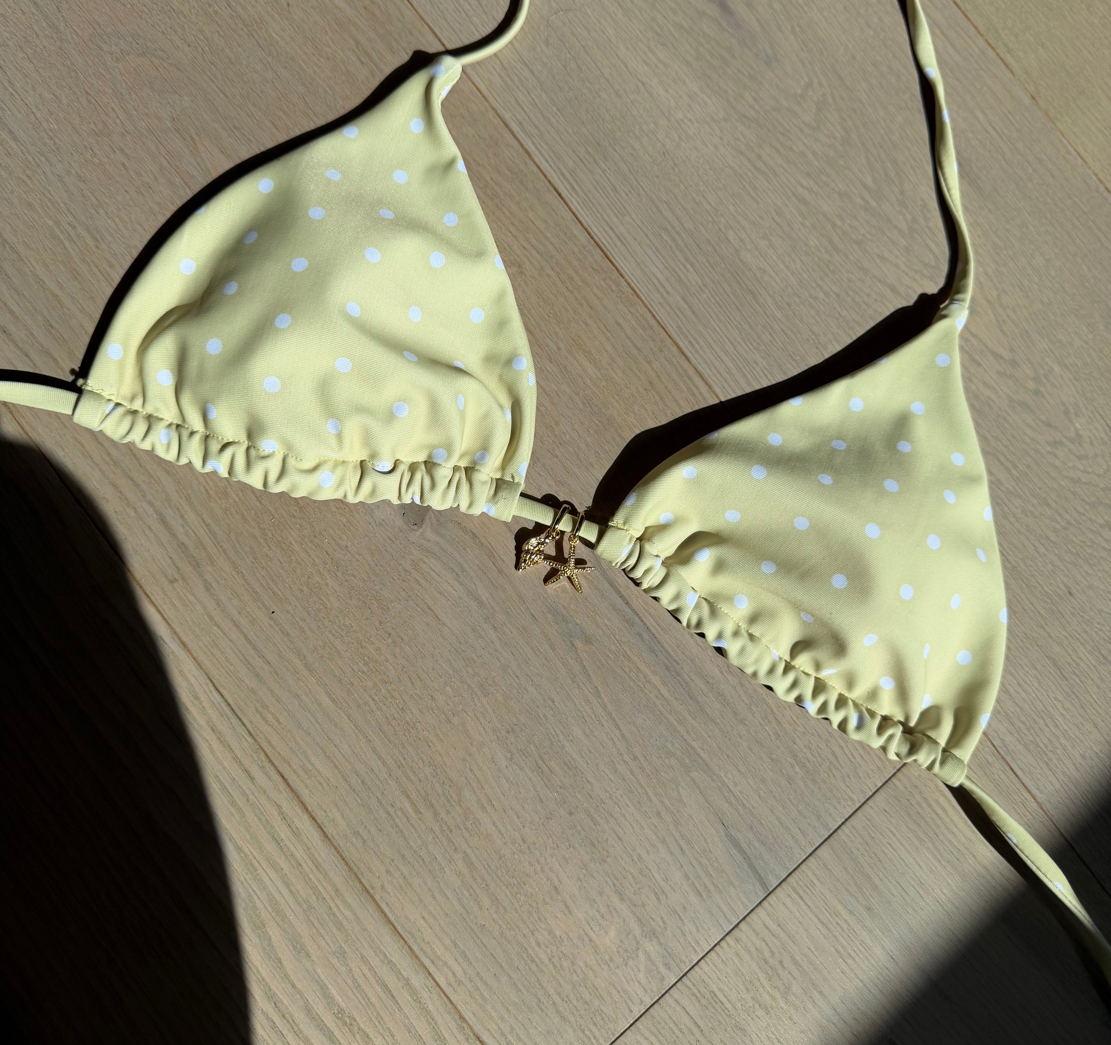 Yellow bikini with white polka dots and gold bikini charms on a wooden floor