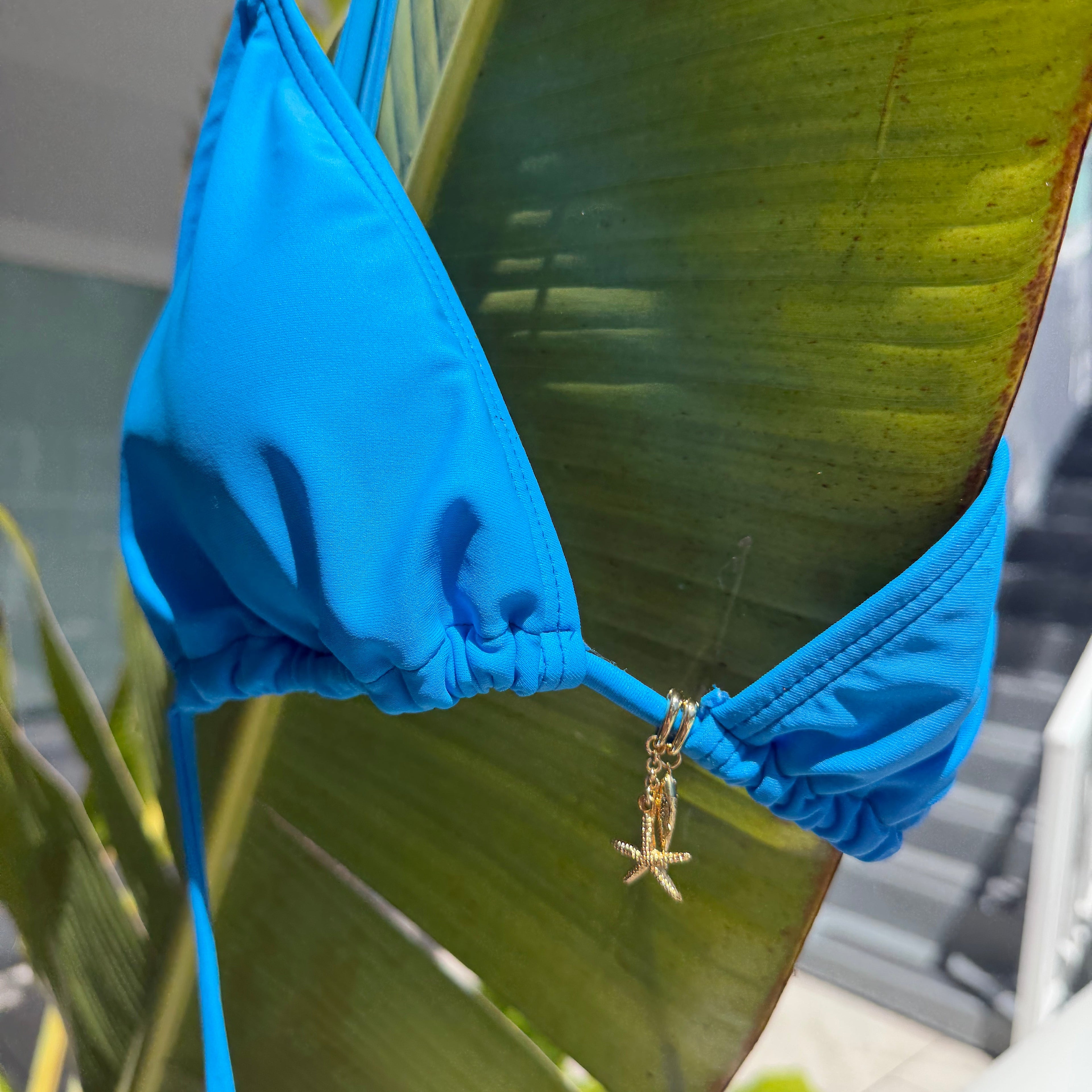 Blue bikini top on a green leaf with a gold starfish bikini charm